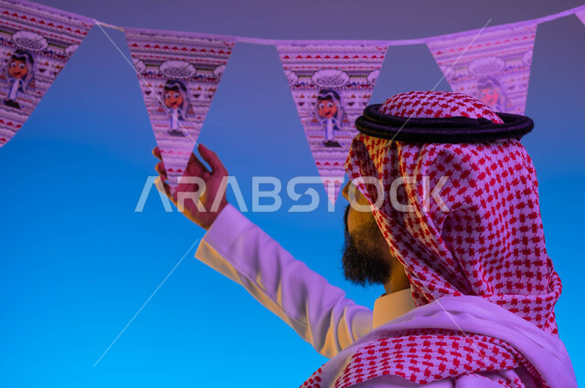 صورة مقربة لرجل عربي خليجي سعودي يمسك زينة العيد، بهجه وفرحة العيد، استقبال العيد، الاحتفال بالعيد السعيد، أعياد ومناسبات، خلفية ملونة 