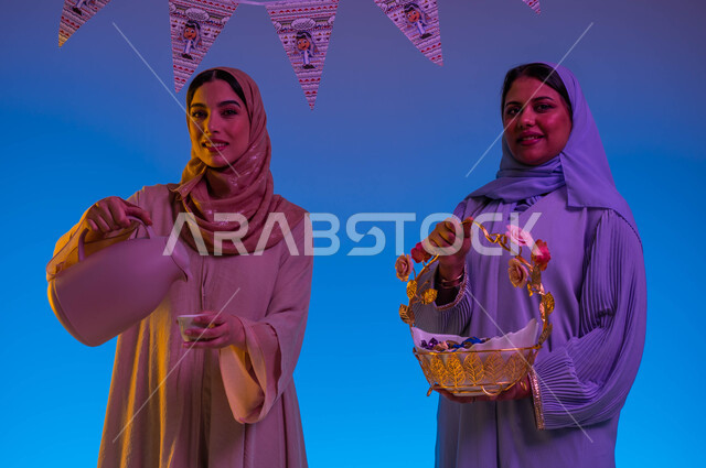 سيدتان خليجيتان سعوديتان عربيتان يحملن ضيافة العيد، تقديم القهوة الساخنة، الحلوى والقرقيعان، اجواء العائلة السعودية في العيد، حسن الضيافة والإستقبال، زيارات العيد، العيد بين الأهل، ايماءات وجه مبتسمة، الاحتفال بالعيد السعيد، أعياد ومناسبات، خلفية ملونة