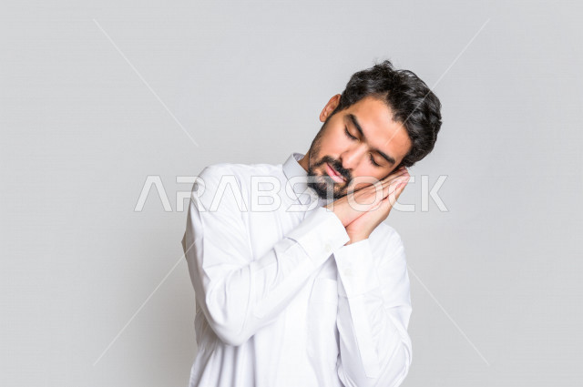 بورتريه لرجل عربي سعودي خليجي يرتدي الثوب السعودي, إيماءات وجه ويدين تدل على النعاس , الشعور بالتعب , الحاجه الى النوم والراحه, الإحساس بالإرهاق, الكسل والخمول , النوم بعمق , خلفية بيضاء .
