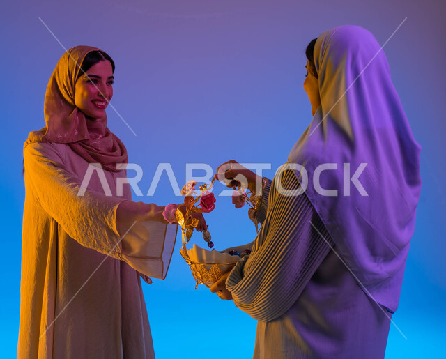 بورتريه لامرأتان سعوديتان عربيتان خليجيتان، زيارات العيد، تقديم حلوى العيد، العيد بين الأهل، بهجه وفرحة العيد، عادات العيد في المجتمع السعودي الخليجي، الاحتفال بالعيد السعيد، الحلوى والقرقيعان، أعياد ومناسبات، خلفية ملونة