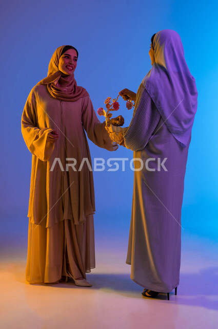Portrait of two Saudi Arab Gulf women, presenting Eid sweets, Eid between the family, joy and joy of Eid, Eid customs in the Saudi Gulf society, Eid visits, celebrating the happy Eid, sweets and Qirqe’an, holidays and occasions, colorful background