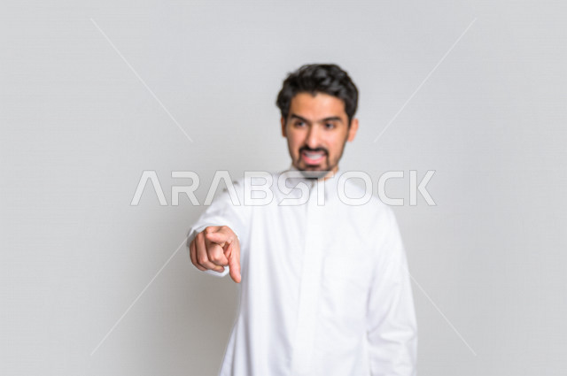 بورتريه لرجل عربي سعودي خليجي باللباس السعودي التقليدي ,  إشارات يدين تدل على العصبية والإشارة الى شخص ما , إيماءات وجه و يدين تدل على الغضب ، الإشارة بإصبع السبابة الى شيء ما , خلفية بيضاء .