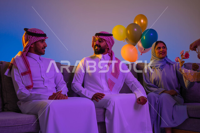 لمة لعائلة سعودية في العيد، امرأة عربية خليجية سعودية تقدم حلوى العيد، العيد بين الأهل، عائلة عربية خليجية سعودية في غرفة المعيشة، بهجه وفرحة العيد، اللمة العائلية، العيد في المجتمع السعودي، زيارات العيد، الاحتفال بالعيد السعيد، أعياد ومناسبات