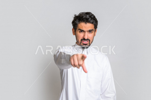 بورتريه لرجل عربي سعودي خليجي باللباس السعودي التقليدي ,  إشارات يدين تدل على العصبية والإشارة الى شخص ما , إيماءات وجه و يدين تدل على الغضب ، الإشارة بإصبع السبابة الى شيء ما , خلفية بيضاء .