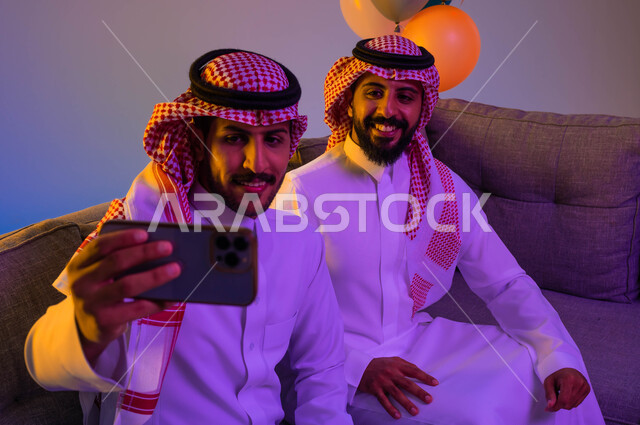 صورة مقربة لرجلان عربيان خليجيان سعوديان يلتقطان صور سيلفي تذكارية، استخدام الهاتف المحمول، الكاميرا الامامية، ايماءات وجه سعيدة، اجواء العيد، زيارات العيد، الاحتفال بالعيد السعيد، أعياد ومناسبات