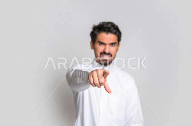 بورتريه لرجل عربي سعودي خليجي باللباس السعودي التقليدي ,  إشارات يدين تدل على العصبية والإشارة الى شخص ما , إيماءات وجه و يدين تدل على الغضب ، الإشارة بإصبع السبابة الى شيء ما , خلفية بيضاء .