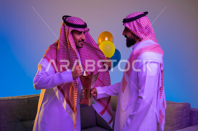 رجلان عربيان خليجيان سعوديان يستخدمان المبخرة، حامل البخور، استخدام خشب العود في المناسبات الاجتماعية والدينية، التطيب والتعطر، العيد في المجتمع السعودي، بهجة وفرحة العيد، الاحتفال بالعيد السعيد