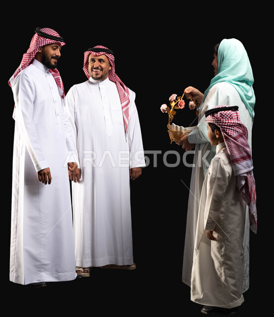 سلة مليئه بقرقيعان وتوزيعات العيد ، بورتريه لعائلة عربية خليجية سعودية ترتدي الزي التقليدي السعودي ، إيماءات وجه تدل على الفرح والسعادة ،أجواء العيد في السعودية ، صورة الجسم بالطول الكامل ، الاحتفال في أيام العيد السعيد ، خلفية سوداء