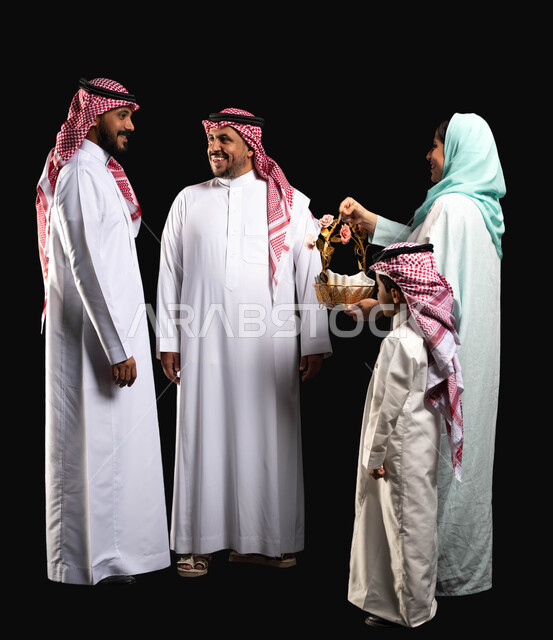 بورتريه لعائلة عربية خليجية سعودية ترتدي الزي التقليدي السعودي ، إيماءات وجه تدل على الفرح والسعادة ،أجواء العيد في السعودية ، صورة الجسم بالطول الكامل ، الاحتفال في أيام العيد السعيد, سلة مليئه بقرقيعان وتوزيعات العيد ، خلفية سوداء