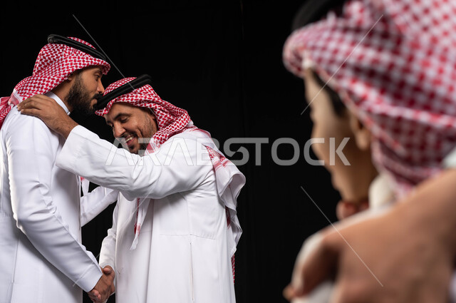 أجواء عائليه سعيده ، بورتريه مقرب لرجل عربي سعودي خليجي يرتدي الزي السعودي التقليدي يقوم بتقبيل رأس جده , عيد مبارك, المناسبات والاعياد الاسلاميه, التجمعات الأسريه في العيد السعيد ، صورة الجسم بالطول الكامل ، خلفيه سوداء