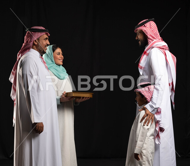 زيارات وتجمعات عائليه ، بورتريه لعائلة عربية خليجية سعودية ، تقديم الضيافة وحلوى العيد ،شابة عربيه سعوديه خليجيه تقوم بتقديم حلوى العيد للضيوف ، مناسبات واعياد اسلاميه, اكرام الضيف وحسن الاستقبال, خلفيه سوداء