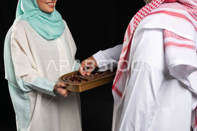 زيارات وتجمعات عائليه ، بورتريه لامراه عربيه سعوديه خليجيه تقوم بتقديم حلوى العيد للضيوف, مناسبات واعياد اسلاميه, اكرام الضيف وحسن الاستقبال, خلفيه سوداء
