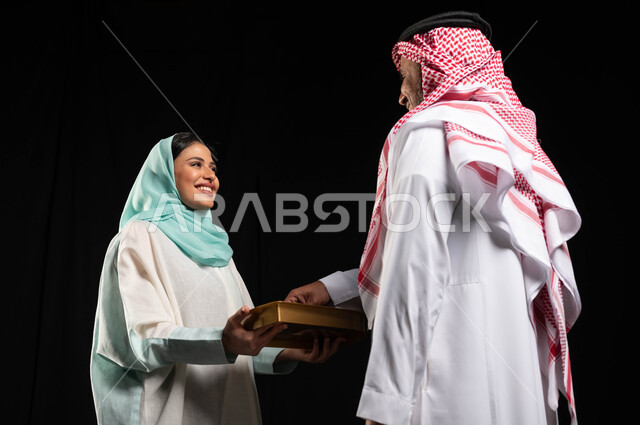 بورتريه لامراه عربيه سعوديه خليجيه تقوم بتقديم حلوى العيد للضيوف, مناسبات واعياد اسلاميه, زيارات وتجمعات عائليه, اكرام الضيف وحسن الاستقبال, خلفيه سوداء