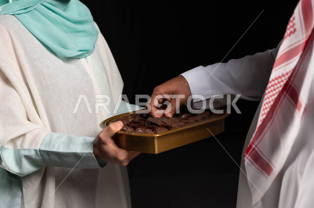 بورتريه مقرب لامراه عربيه سعوديه خليجيه تقوم بتقديم حلوى العيد للضيوف, مناسبات واعياد اسلاميه, زيارات وتجمعات عائليه, اكرام الضيف وحسن الاستقبال, خلفيه سوداء