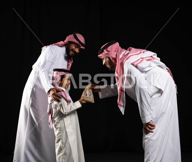 تقديم العيدية للأطفال ، بورتريه لعائلة عربية سعودية خليجية ترتدي الثوب والشماغ السعودي , ايماءات تدل على الحب والاهتمام بالاولاد, ارتداء الزي السعودي التقليدي في الأعياد والمناسبات, أجواء عائليه سعيده, عيد مبارك, خلفيه سوداء