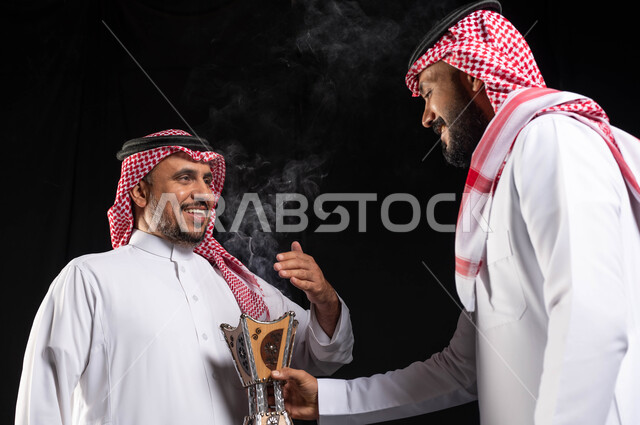 الاحتفال بقدوم العيد ، استخدام خشب العود ، زيارات العيد ، حامل البخور( المبخرة ) ، بورتريه لرجلان عربيان خليجيان سعوديان يرتديان الزي السعودي التقليدي ، أجواء العيد في السعودية ، التطيب والتعطر ، خلفية سوداء