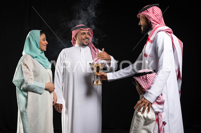 التطيب والتعطر ، أجواء العيد في السعودية ، بورتريه لأمرأه عربية خليجية سعودية محجبة تحمل حامل البخور( المبخرة ) ، رجل عربي خليجي سعودي يرتدي الزي التقليدي السعودي ، استخدام خشب العود في المناسبات الاجتماعية ، خلفية سوداء