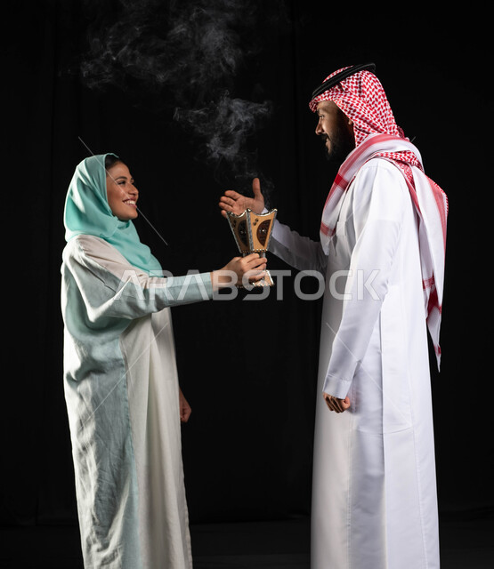التطيب والتعطر, الاستعداد للخروج ، بورتريه لشابة عربية خليجية سعودية محجبة تحمل حامل البخور( المبخرة ) ، رجل عربي خليجي سعودي يرتدي الزي التقليدي السعودي ،  استخدام خشب العود في المناسبات الاجتماعية و الدينية ، خلفية سوداء
