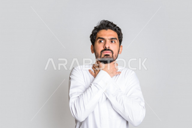 Portrait of a Saudi Arabian Gulf man wearing the Saudi dress, making facial and hand gestures indicating suffocation and feeling short of breath, mental illness, depression, suicide, feeling insecure, white background.