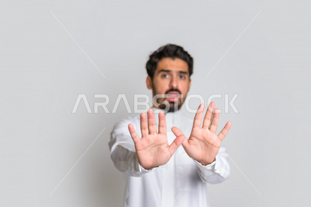 بورتريه لرجل عربي سعودي خليجي يرتدي الثوب السعودي, إيماءات يدين تدل على الأمر بالتوقف عن فعل شيء ما, الشعور بالخوف و الإنزعاج, الرفض والإمتناع , خلفية بيضاء .
