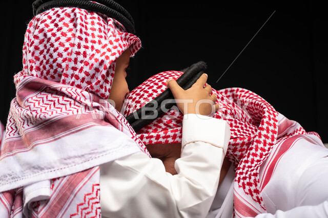 التجمعات الأسريه في العيد السعيد, بورتريه مقرب لطفل عربي سعودي خليجي يرتدي الزي السعودي التقليدي يقوم بتقبيل رأس جده , أجواء عائليه سعيده, عيد مبارك, المناسبات والاعياد الاسلاميه, خلفيه سوداء