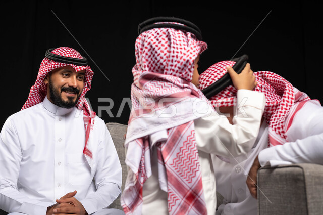بورتريه مقرب لطفل عربي سعودي خليجي يرتدي الزي السعودي التقليدي يقوم بتقبيل رأس جده ، التجمعات الأسريه في العيد السعيد , أجواء عائليه سعيده, عيد مبارك, المناسبات والاعياد الاسلاميه, خلفيه سوداء