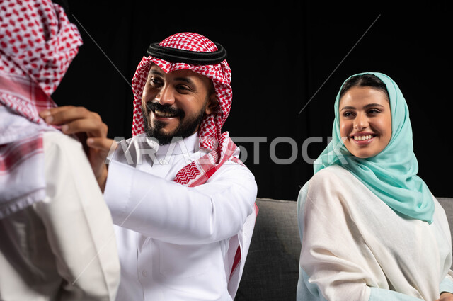 بورتريه لأب عربي سعودي خليجي يرتدي الزي السعودي التقليدي يقوم بمساعدة ابنه على ارتداء ملابس العيد, التهيؤ والتحضير للعيد السعيد, أجواء عائليه سعيده, أعياد ومناسبات اسلاميه , خلفيه سوداء
