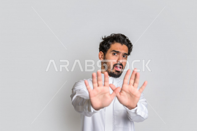بورتريه لرجل عربي سعودي خليجي يرتدي الثوب السعودي, إيماءات يدين تدل على الأمر بالتوقف عن فعل شيء ما, الشعور بالخوف و الإنزعاج, الرفض والإمتناع , خلفية بيضاء .