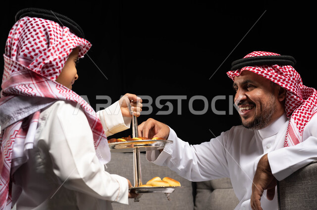 ايماءات تدل على الفرح والسعاده ، بورتريه لرجل عربي سعودي خليجي يرتدي الزي السعودي التقليدي , تقديم حلوى وكعك العيد , حسن استقبال واكرام الضيوف, الزيارات و التجمعات الاسريه, أعياد ومناسبات, التهنئه بقدوم العيد, خلفيه سوداء