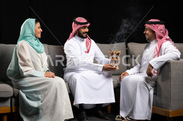 التطيب بالبخور والعود ، استخدام خشب العود في المناسبات والأعياد ، عائلة عربية خليجية سعودية تحتفل بالعيد ، الزيارات العائلية والتجمعات الأسرية ، خلفية سوداء