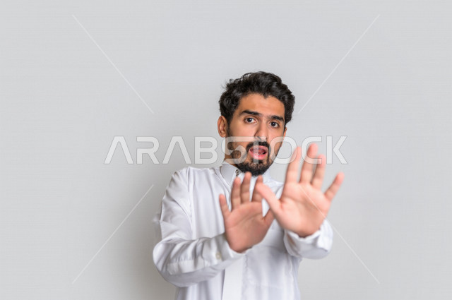 بورتريه لرجل عربي سعودي خليجي يرتدي الثوب السعودي, إيماءات يدين تدل على الأمر بالتوقف عن فعل شيء ما, الشعور بالخوف و الإنزعاج, الرفض والإمتناع , خلفية بيضاء .