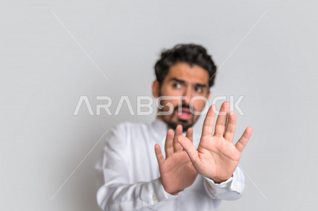 بورتريه لرجل عربي سعودي خليجي يرتدي الثوب السعودي, إيماءات يدين تدل على الأمر بالتوقف عن فعل شيء ما, الشعور بالخوف و الإنزعاج, الرفض والإمتناع , خلفية بيضاء .