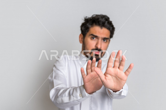 بورتريه لرجل عربي سعودي خليجي يرتدي الثوب السعودي, إيماءات يدين تدل على الأمر بالتوقف عن فعل شيء ما, الشعور بالخوف و الإنزعاج, الرفض والإمتناع , خلفية بيضاء .