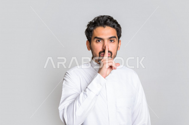 بورتريه لرجل عربي سعودي خليجي باللباس التقليدي ,يقوم بإيماءات وجه مختلفة  ، إشارات يدين تدل على السكوت والكتمان , عدم الإزعاج, التوقف عن الكلام والهدوء , الأمر بالصمت والسكوت , خلفية بيضاء .