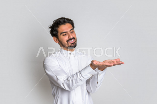 بورتريه لرجل عربي سعودي خليجي باللباس التقليدي , إيماءات وجه مختلفة ، إشارات يدين تدل على حمل شيء ما ، خلفية بيضاء .