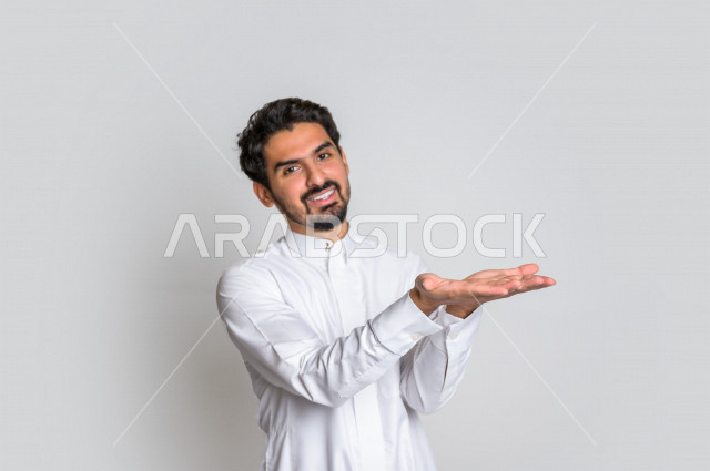 بورتريه لرجل عربي سعودي خليجي باللباس التقليدي , إيماءات وجه مختلفة ، إشارات يدين تدل على حمل شيء ما ، خلفية بيضاء .