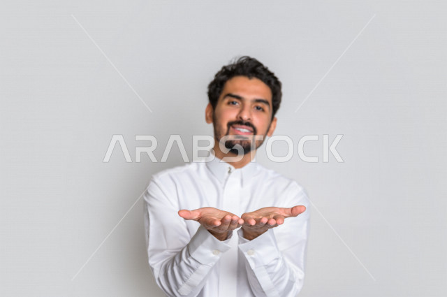 بورتريه لرجل عربي سعودي خليجي باللباس التقليدي , إيماءات وجه مختلفة ، إشارات يدين تدل على حمل شيء ما ، خلفية بيضاء .