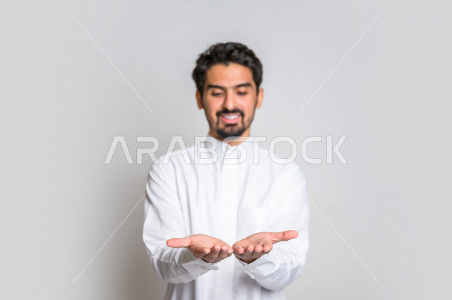 بورتريه لرجل عربي سعودي خليجي باللباس التقليدي , إيماءات وجه مختلفة ، إشارات يدين تدل على حمل شيء ما ، خلفية بيضاء .