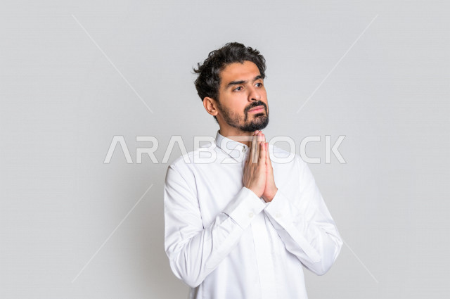 Portrait of a Saudi Arabian Gulf man, wearing traditional Saudi dress, raising his hands up and supplicating to God with different facial and hands gestures denoting supplication and supplication, concept of supplication and need, worship and getting clos