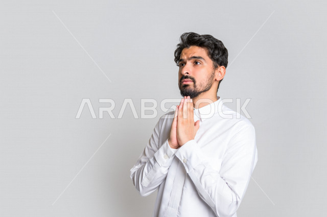 Portrait of a Saudi Arabian Gulf man, wearing traditional Saudi dress, raising his hands up and supplicating to God with different facial and hands gestures denoting supplication and supplication, concept of supplication and need, worship and getting clos
