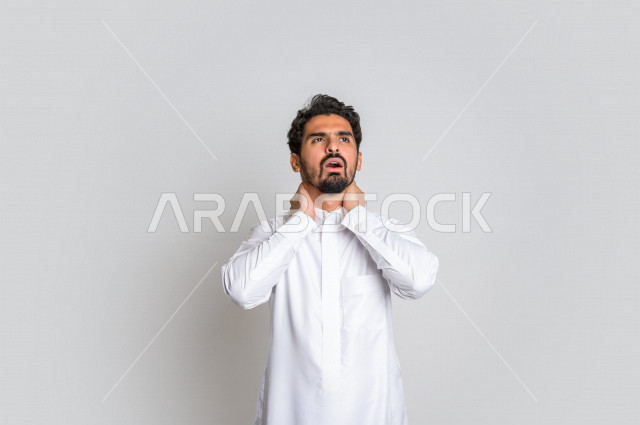 بورتريه لرجل عربي سعودي خليجي باللباس التقليدي , يقوم بإيماءات وجه تدل على الوجع والألم ، إشارات يدين تدل على التعب والوجع بالرقبة ، خلفية بيضاء .