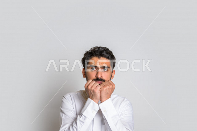 بورتريه لرجل عربي سعودي خليجي يشعر بالخوف بإيماءات وجه مختلفة ، إشارات يدين تدل على الهلع ، خلفية بيضاء .