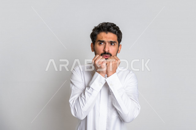 بورتريه لرجل عربي سعودي خليجي يشعر بالخوف بإيماءات وجه مختلفة ، إشارات يدين تدل على الهلع ، خلفية بيضاء .
