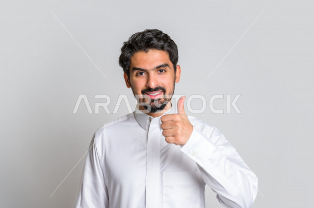بورتريه لرجل عربي سعودي خليجي باللباس التقليدي , يقوم بإيماءات وجه تدل على السعادة ، إشارات يدين تدل على الفرحة بالفوز ، خلفية بيضاء .
