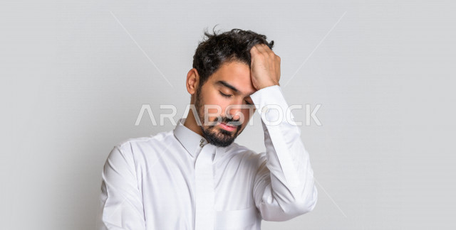 Portrait of a Saudi Arabian Gulf man in traditional dress, making facial gestures indicating nervousness and remorse, hand gestures indicating loss and failure, white background.