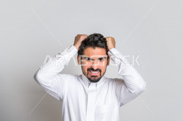 Portrait of a Saudi Arabian Gulf man in traditional dress, making facial gestures indicating nervousness and remorse, hand gestures indicating loss and failure, white background.
