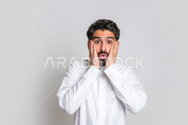 بورتريه لرجل عربي سعودي خليجي باللباس التقليدي , يقوم بإيماءات وجه و يدين تدل على الدهشة و الذهول , الصدمة بسماع الخبر ، خلفية بيضاء .
