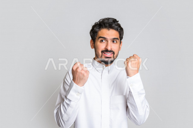 بورتريه لرجل عربي سعودي خليجي باللباس التقليدي , يقوم بإيماءات وجه تدل على السعادة ، إشارات يدين تدل على الفرحة بالفوز ، خلفية بيضاء .