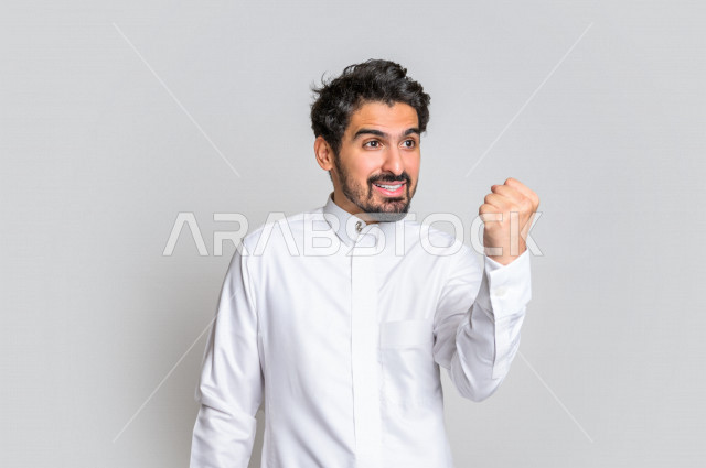 Portrait of a Saudi Arabian Gulf man in traditional dress, making facial gestures indicating happiness, hand gestures indicating happiness, white background.