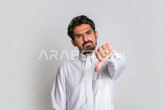 بورتريه رجل عربي سعودي خليجي باللباس التقليدي , يقوم بإيماءات وجه تدل على الندم , إشارات يد تدل على الخسارة والفشل , خلفية بيضاء .